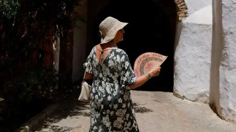 Reuters A woman uses a hand fan to cool off during the first summer heatwave in Seville