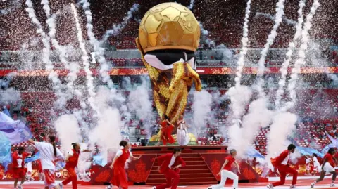 Singers Elyanna and Jessie Reyez perform during the opening ceremony. They are on a stage with a replica gold world cup and are dressed in colourful clothing