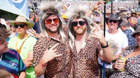 PA Media Two men dressed to look like Rod Stewart are standing in a crowd. They are both wearing wigs and leopard print shirts.