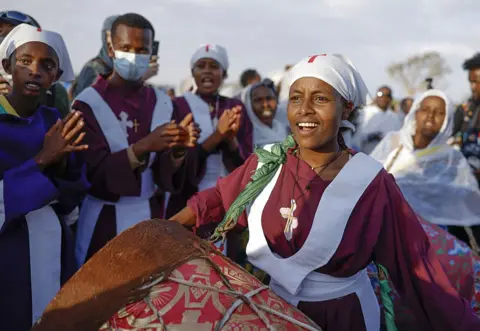 Anadolu via Getty Images A woman in a purple top chants an bangs a drum.