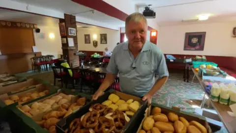 man in blue polo top standing behind trays of pastries