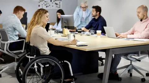 Getty Images Wheelchair using young woman takes notes in a meeting