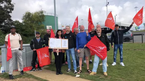 Kate Bradbrook/BBC Workers holding flags and posters striking over pay and working conditions at Luton airport