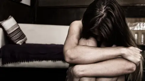Getty Images A woman sitting with her arms around her legs