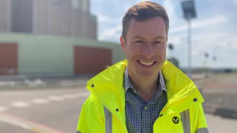 Magnox Ltd project manager Adam Jones wearing a hi vis jacket smiling at the camera