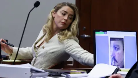 Getty Images Actress Amber Heard listens to her ex-husband Johnny Depp, as a picture of an injury to his face is seen on a screen, during his defamation trial against her at the Fairfax County Circuit Courthouse in Fairfax, Virginia, April 20, 2022