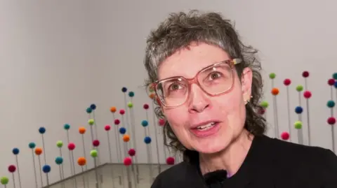 Sonia Boué in front of an display of multi-coloured round pop poms 