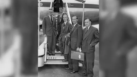 Keystone/Hulton Archive/Getty Images Black and white image of James Sayers (second from right) leaving London Airport with other scientists. James is carrying a bag. The three others beside him are standing on the steps of the plane