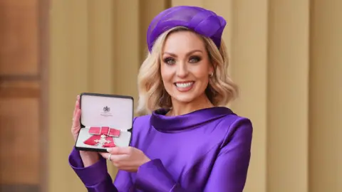 Dancer and television presenter Amy Dowden wears a purple dress and hat after being made an MBE (Member of the Order of the British Empire) during an Investiture ceremony at Buckingham Palace on 18 February, 2025.