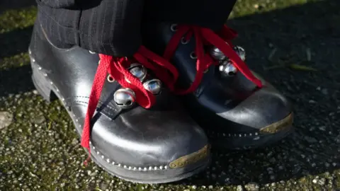 A close up photo of some traditional black clogs with red shoe laces with silver bells attached to them. 