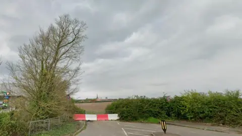 Google Field with bushes and trees around the border and a red and white barrier preventing access