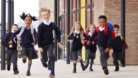 Seven pupils in school uniform happily running towards the camera