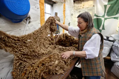 Colin Hattersley Artist Rebecca McLellan in her workshop looking at a large brown sheep's fleece