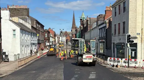 Road resurfacing work on Buccleuch Street in Dumfries with workmen on the road and machinery to put down and roll new asphalt