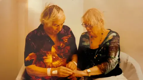 Worcestershire Acute Hospitals NHS Trust A man and a woman, both in dark-coloured tops with a flowery design are sat down in a beige room whole the man places a ring on the woman's finger