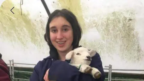 Sharren Bridges A teenage girl with brown hair and braces holds a newly-born lamb