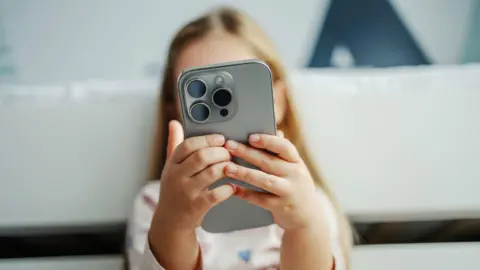 Getty Images Child's hands holding a modern smartphone covering face.