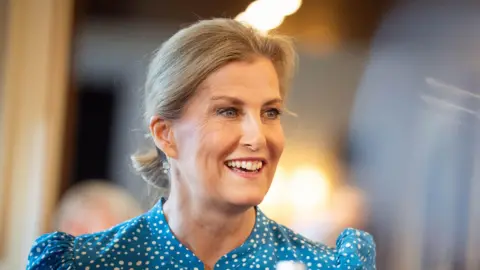 PA Media Sophie, Duchess of Edinburgh has a broad smile on her face while she talks to people at a royal engagement. She is wearing a blue dress with white polka dots on it.