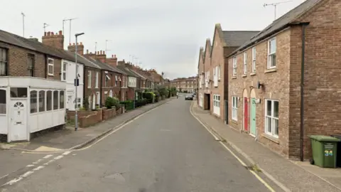 A street with mostly red brick terraced houses on either side. 