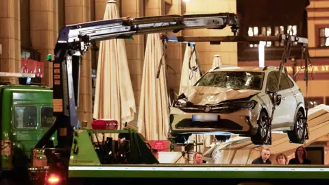 A white car which is damaged at the front is lifted with a crane in Leipzig, Germany,