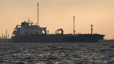 An oil tanker at sea silhouetted against a sky at sunset.