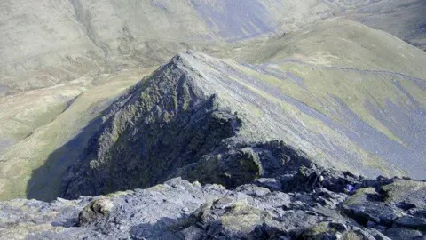 A picture taken from the top of Blencathra looking down at Sharp Edge. The ridge is surrounded by steep drops on either side and is very rocky.