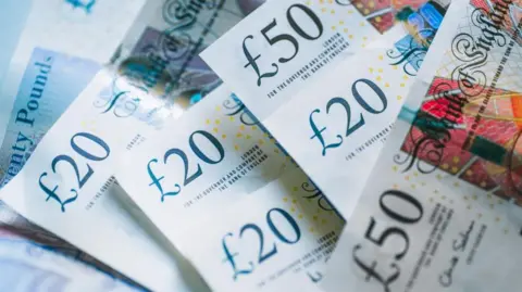 A photo showing a mixture of £20 and £50 notes lying on a table. 