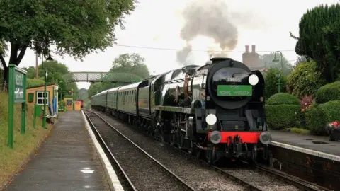 A black steam locomotive sits in the station at Four Marks