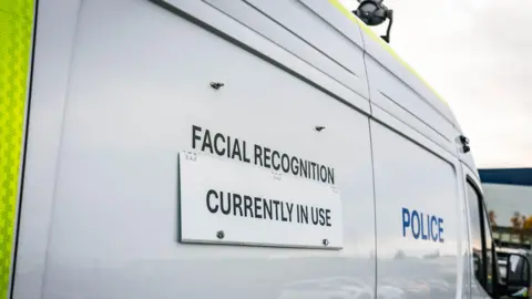 Merseyside Police The side of a white police van with a sign reading 'Facial Recognition Currently in Use' 