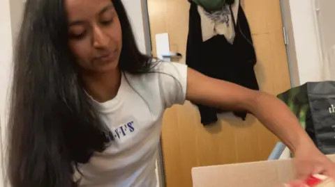 BBC/Seb Cheer A young woman, Geena, puts a book into a cardboard box as she packs up her belongings in a student flat.