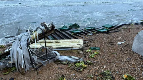 Gavin Jones Large sections of bright green plastic crates, clear plastic wrapping and insulation material are pictured at the stony shoreline at Selsey, which is strewn with blackened bananas.