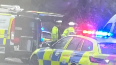 A blurry photo of police officers and a police car on a road. The lights are flashing on the police car