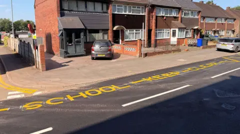 A street with a sign painted in yellow that reads School - Keep - Clear.