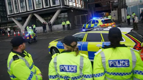 Police officers watching as police escort a prison van