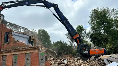 Demolition at the site with a machine pulling down walls