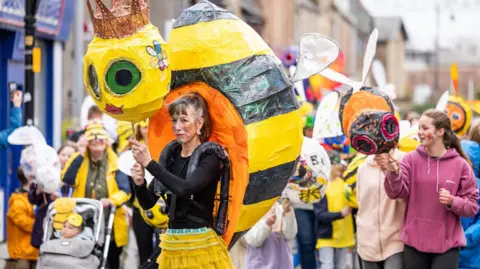 Paul Campbell A woman wears a large puppet of a yellow and black queen bee as she walks in the parade.