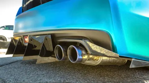 A modified car that has a blue rear bumper and a black diffuser with two metal tailpipes.