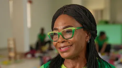 A close-up photo of Nonye Nweke wearing green glasses. She has long hair.