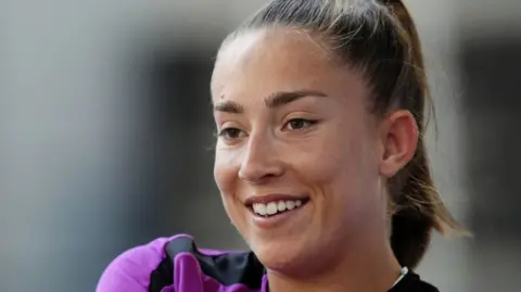 A smiling woman with brown hair and purple shirt