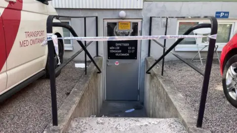 Outdoor stairs lead to a silver door which is taped off with police tape
