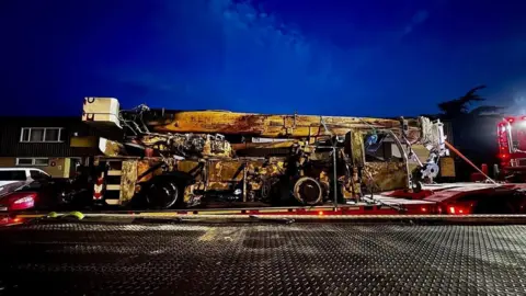 The damaged yellow crane is on the back on a lorry at night