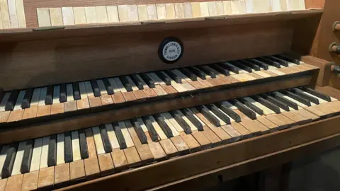 The console of an old pipe organ. The keys are heavily worn, with many showing discolouration and chips.