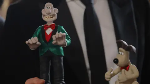 Reuters A man wearing a dark suit and tie holds two small models of Aardman characters Wallace & Gromit