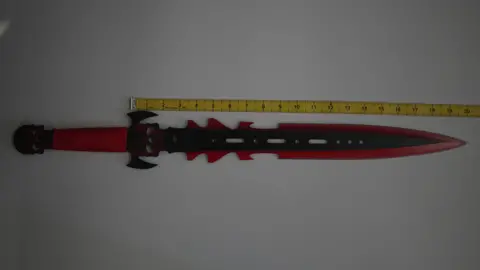 The largest zombie knife lying on a table against a tape measure. The tape measure is against the blade to show the scale of it, at 20 inches (50cm)