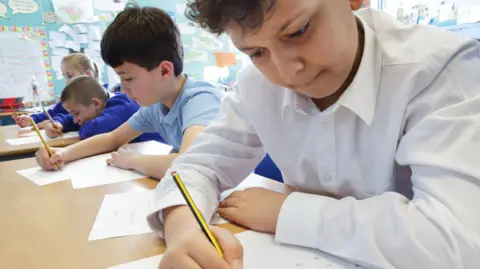 Getty Images A row of primary school students in a classroom with pencils and paper, looking like they are concentrating