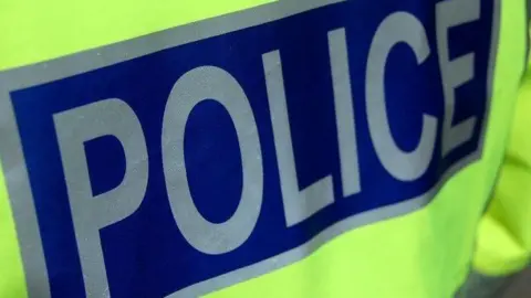 A close up of the back of a police officer's jacket. The word "police" is in silver capital letters on a dark blue background.