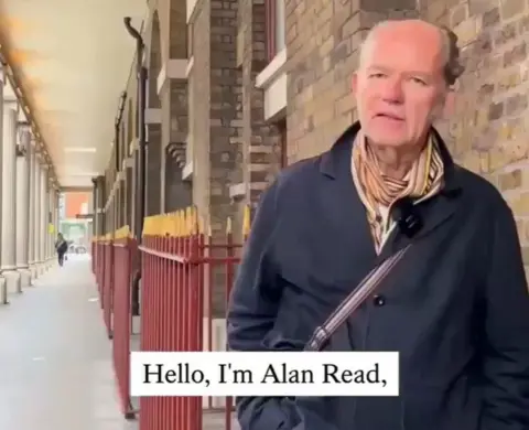Social Media A grab from video depicts Dr Read speaking to the camera while standing outside next to a brick building and red railings, with the text 'hello, I'm Alan Read,' overlain in the bottom as subtitles.