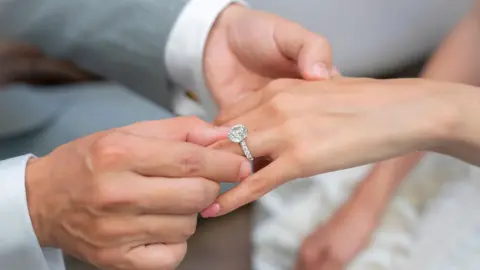 Getty Images A man places an engagement ring with a lab-grown diamond onto his partner's hand