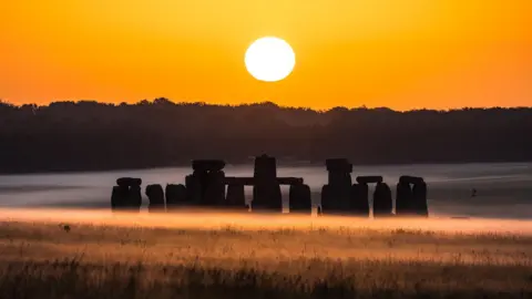 Tom Godber The outlines of the stones at Stonehenge are seen among low morning mist, lit up by a bright sunrise.