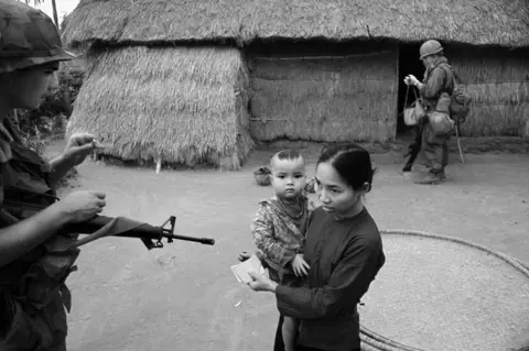 Philip Jones Griffiths/MAGNUM PHOTOS A soldier pointing a gun at a mother and child